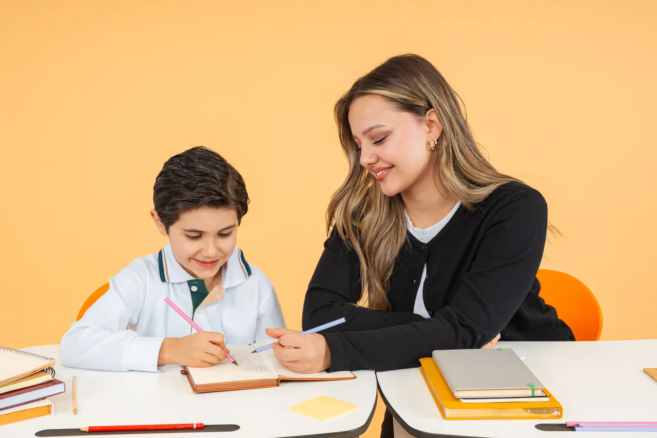 A teacher helping a young student write in a workbook